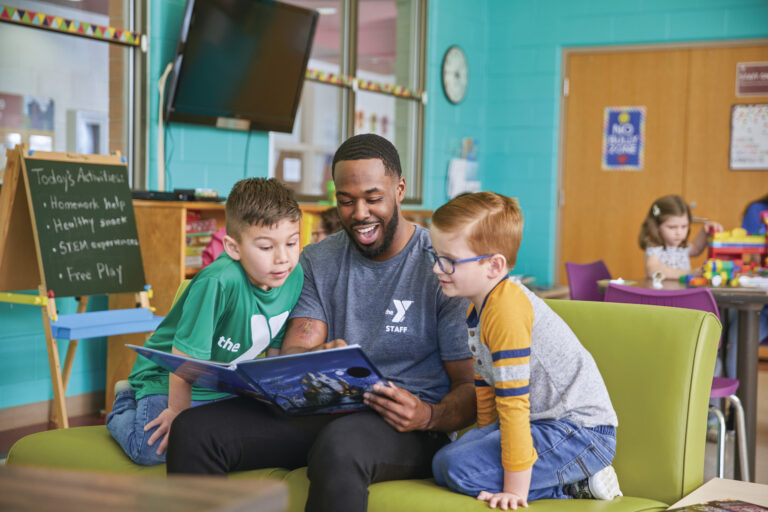 Children and YMCA staffer in classroom reading a book